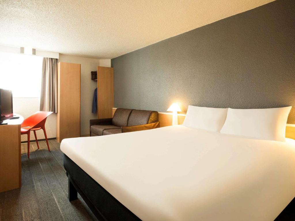 um quarto de hotel com uma grande cama branca e uma cadeira em Ibis Orly Chevilly Tram 7 em Chevilly-Larue
