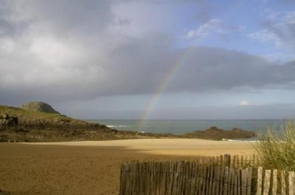 een regenboog in de lucht boven een strand met een hek bij Maison avec jardin et plage de sable fin accessible à pied à 300m in Saint-Coulomb
