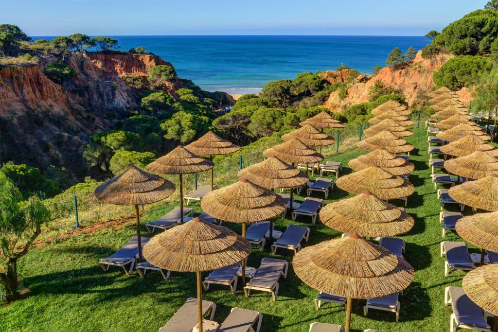 a row of chairs with straw umbrellas and the ocean at 3HB Falésia Garden in Albufeira