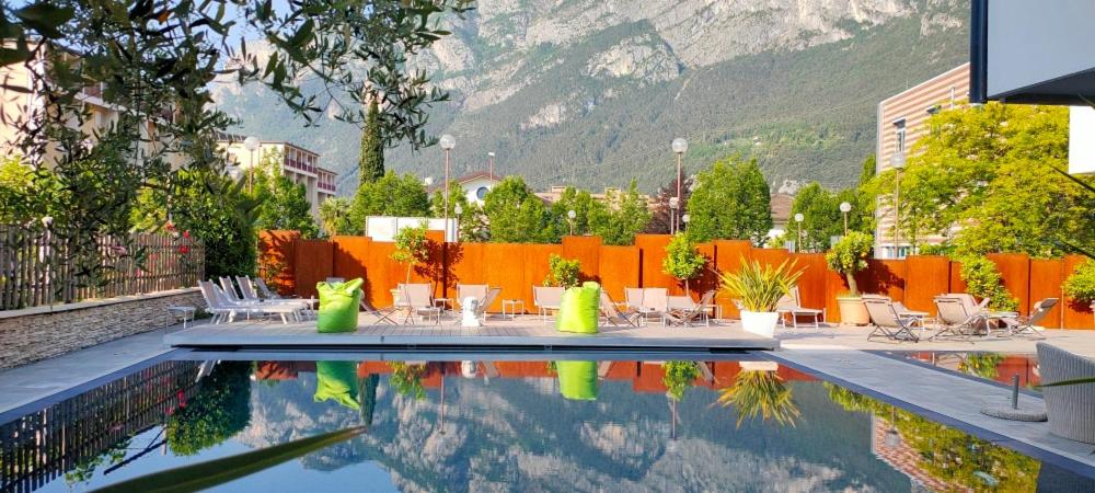una piscina con tavoli, sedie e una montagna di Hotel Virgilio a Riva del Garda