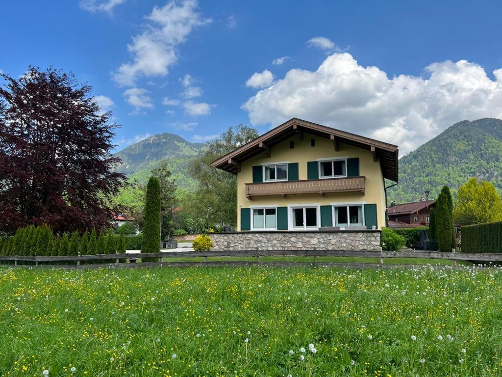 a house in a field with mountains in the background at Villa am Bach in Unterwössen