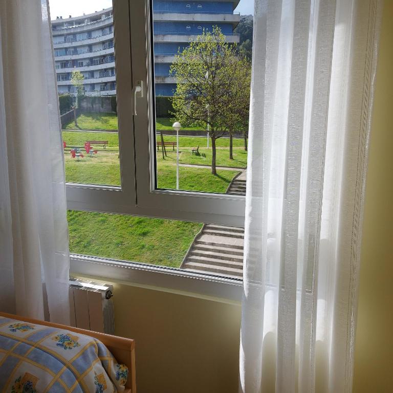 Okno z białymi zasłonami i widokiem na park w obiekcie Bonito piso con garaje y piscina a 8 'centro w mieście Castro-Urdiales
