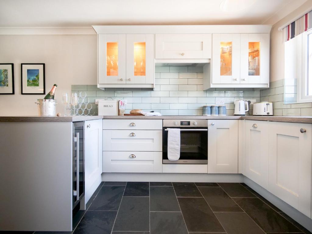 a kitchen with white cabinets and a tile floor at Padstow Escapes - Breakers Holiday Cottage in St Merryn
