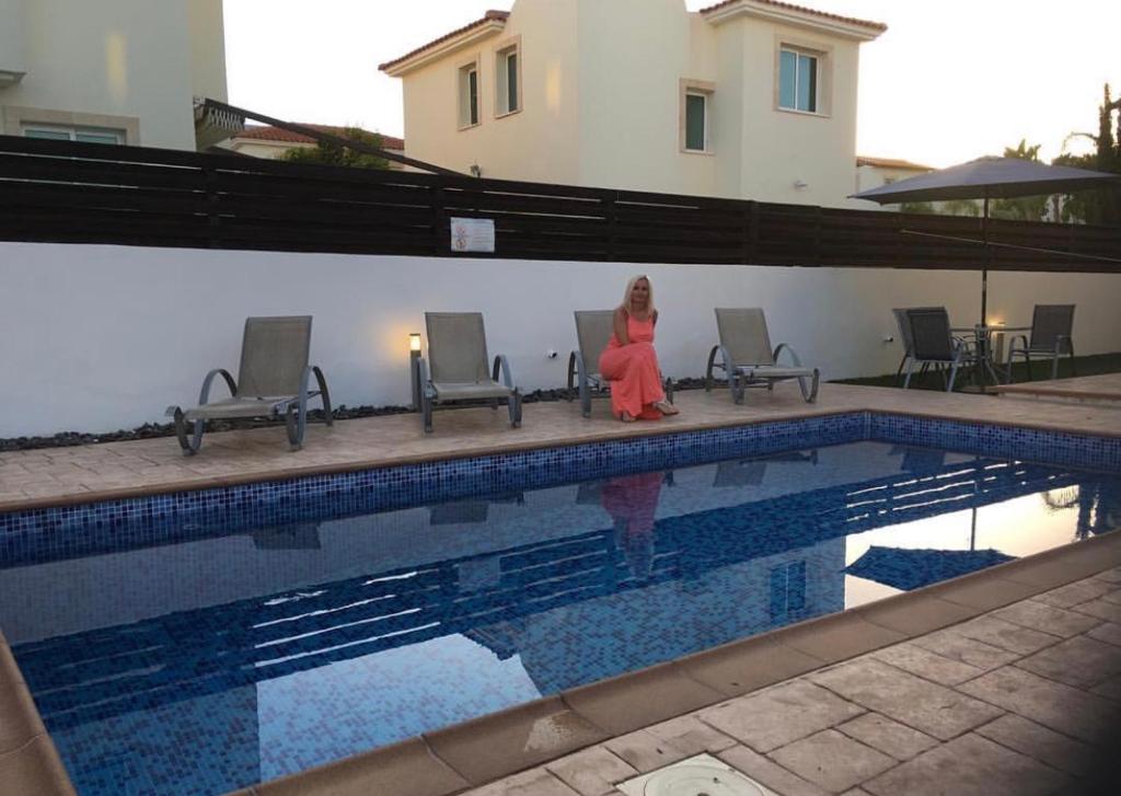 a woman in a red dress sitting next to a swimming pool at Villa millie Cyprus in Protaras