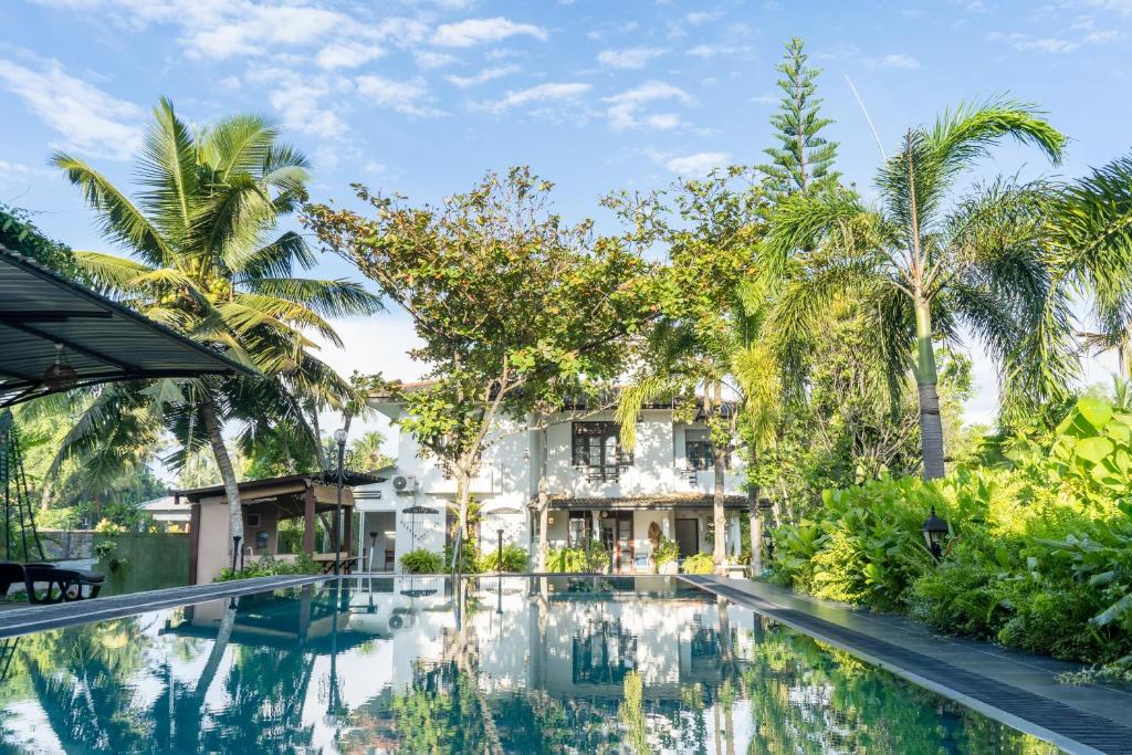 a swimming pool in front of a house with palm trees at Villa Sarakkuwa in Pamunugama