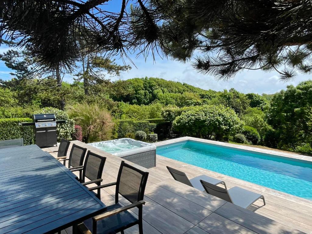 een zwembad naast een tafel en stoelen bij Superbe maison avec piscine et jacuzzi dans les dunes in Ambleteuse