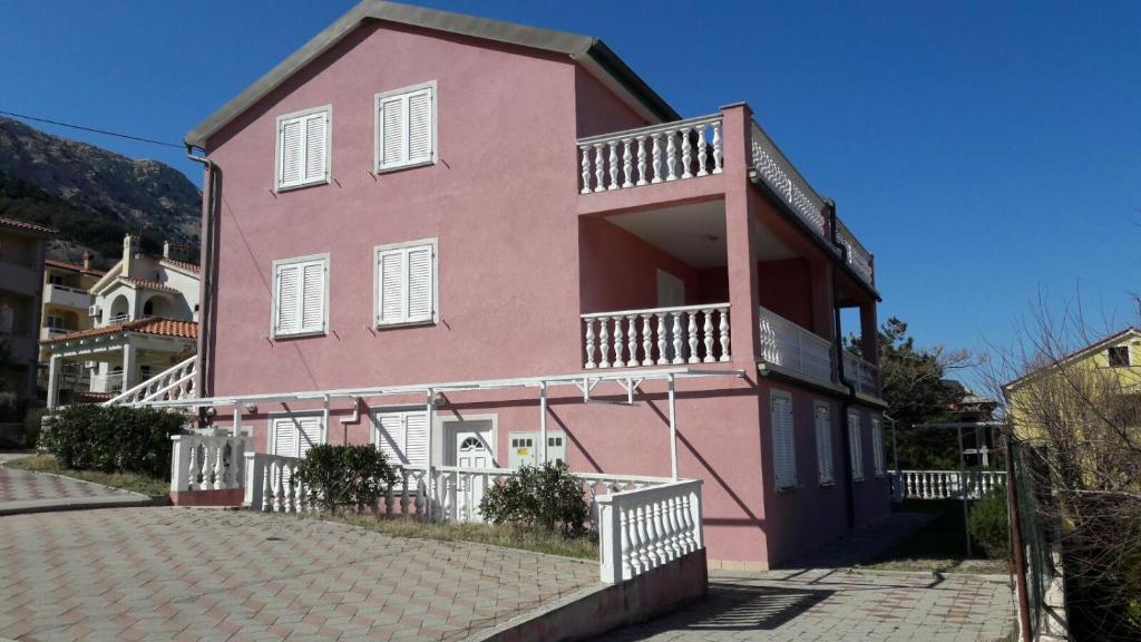 ein rosafarbenes Haus mit Balkon auf einer Straße in der Unterkunft Apartman BoloB in Baška