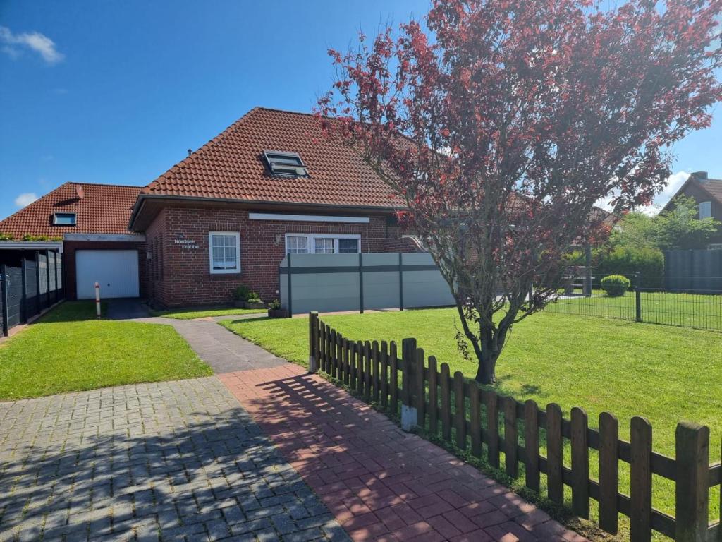 a house with a fence and a tree at Ferienhaus Nordseekrabbe in Norden