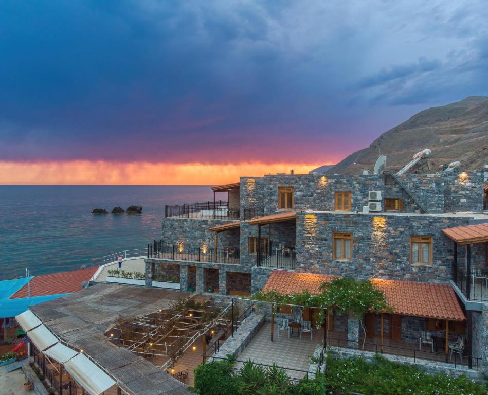 a large stone building next to the ocean at sunset at XENIA HOTEL in Sfakia