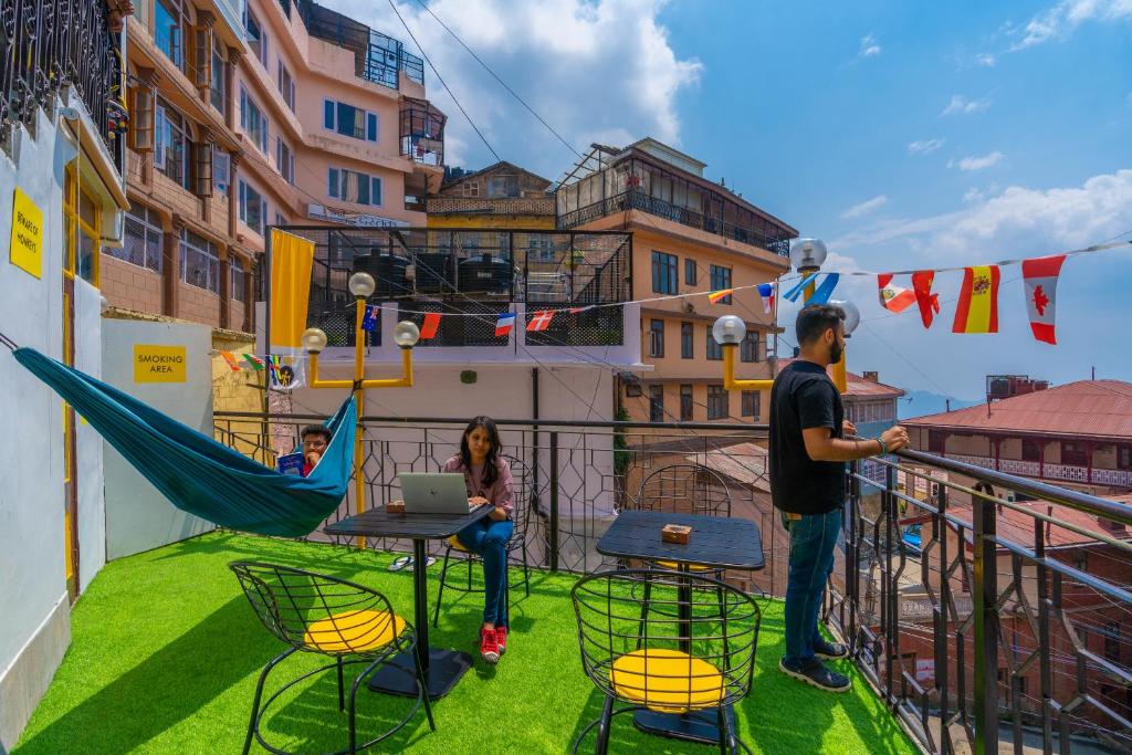 a woman sitting at a table on a balcony with a laptop at The Hosteller Shimla in Shimla