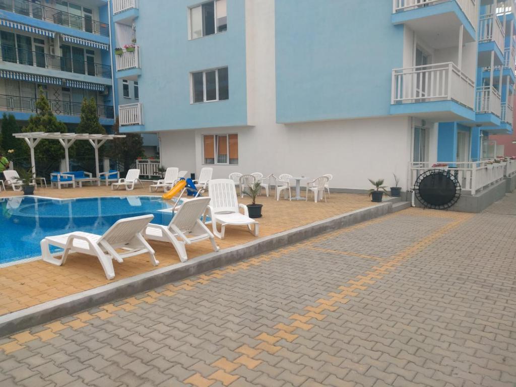uma piscina com cadeiras brancas e um hotel em Blue Sky Apartments em Nesebar