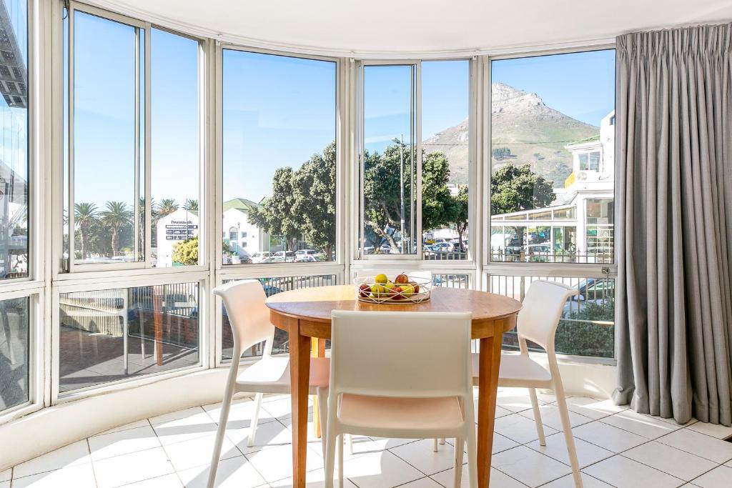 Un comedor con mesa y sillas y grandes ventanales. en Camps Bay Village - Village Apartments, en Ciudad del Cabo