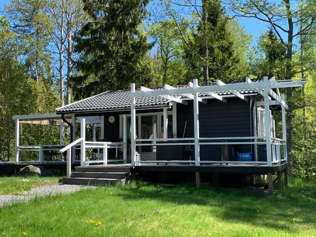 een klein zwart huis met een witte veranda bij Cozy cottage near the sea in Tjustvik