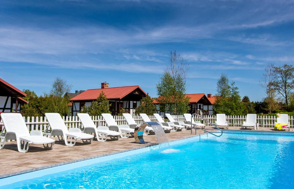 a pool with white lounge chairs and a person standing next to it at Domki Dzika Róża in Darłowo