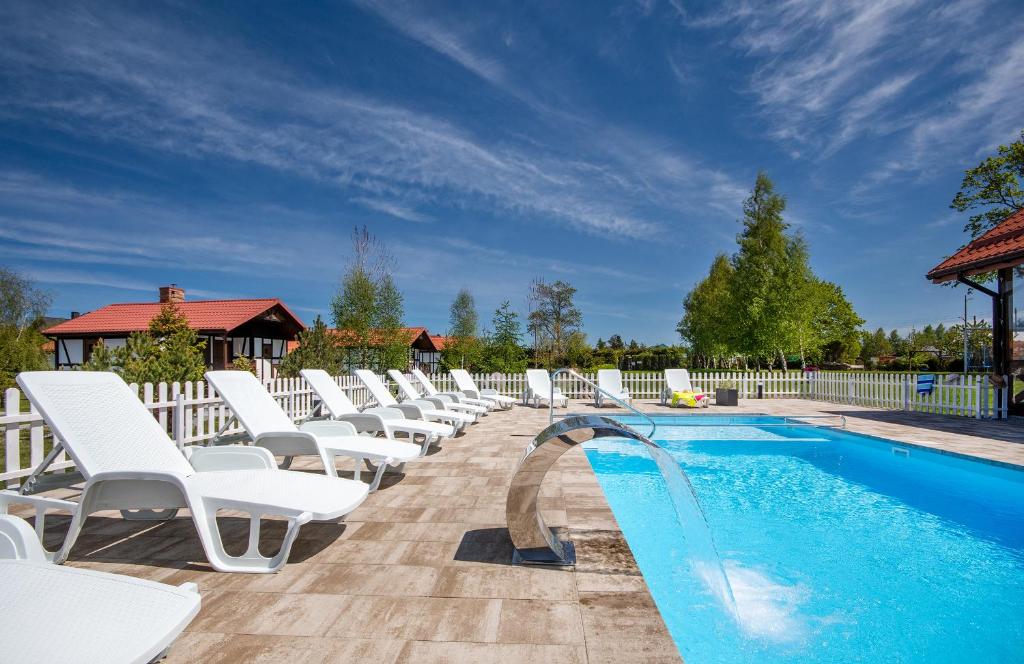 a row of white lounge chairs next to a swimming pool at Kwatery Prywatne Dzika Roza in Darłowo