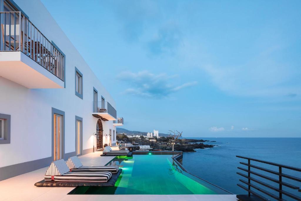 a swimming pool with lounge chairs and the ocean at White Exclusive Suites & Villas in Lagoa