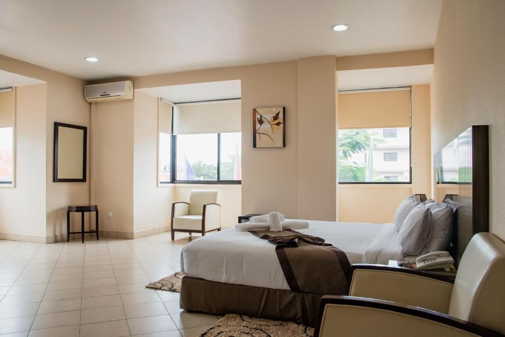 a hotel room with a bed and chairs and windows at Resotel in Maputo