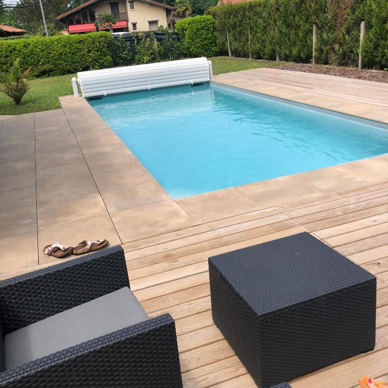 - une piscine avec 2 chaises en osier à côté dans l'établissement Maison landaise moderne avec piscine chauffée et spa, à Lit-et-Mixe