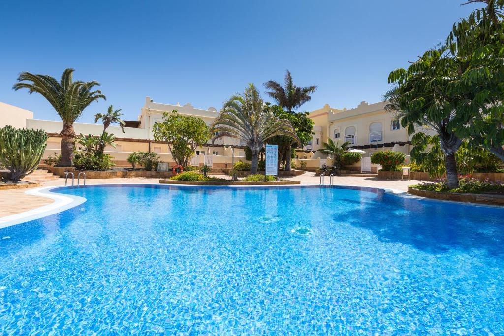 a large swimming pool with palm trees in front of a building at Home2Book Stunning Sultan Casa Estrella, Wifi&Pool in Corralejo