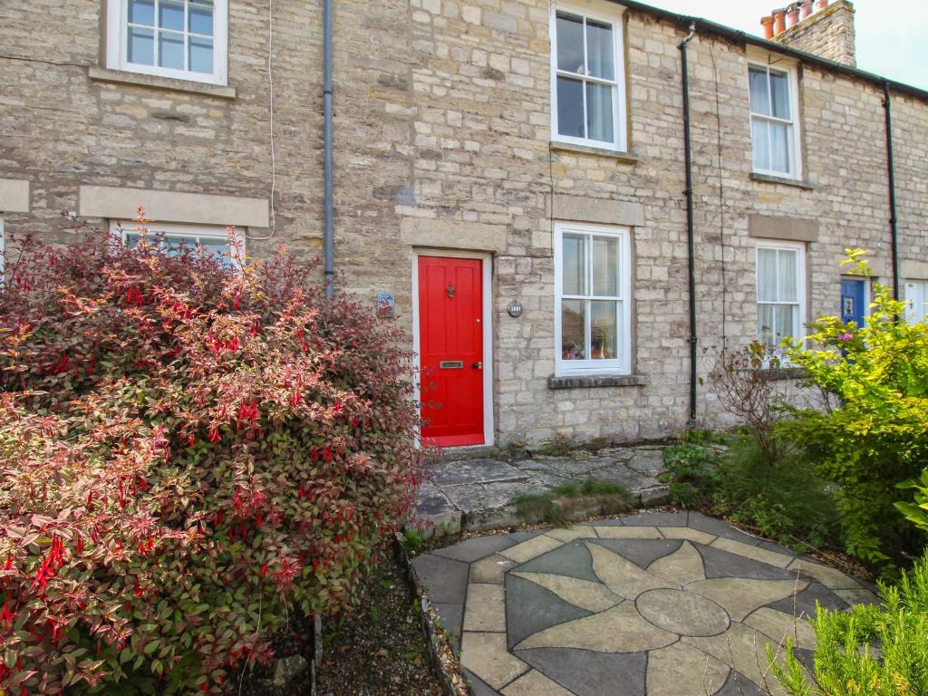 a brick house with a red door and some bushes at Poppy Cottage in Swanage