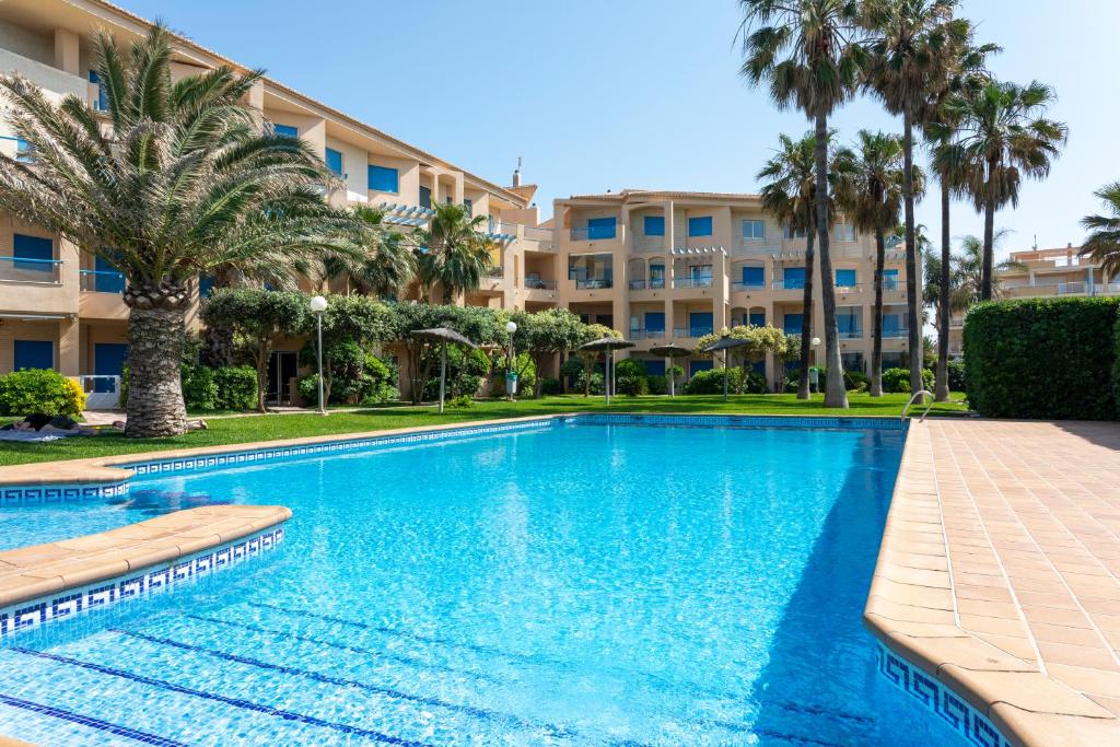 a swimming pool in front of a building with palm trees at Las Dunas, bajo, 2 dormitorios, 25m del mar, by Bookindenia in Denia