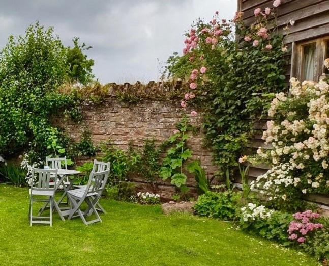 a garden with a table and chairs and a brick wall at The Cottage, Winley Farm in Bromyard
