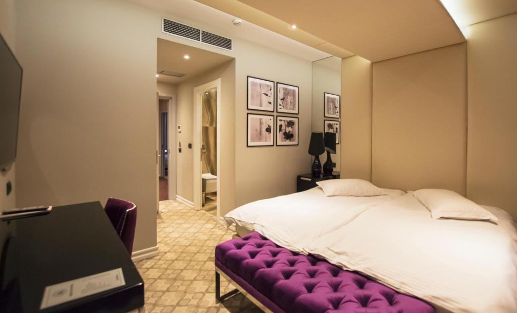 a bedroom with a large bed with a purple bench at Senator Hotel in Tirana
