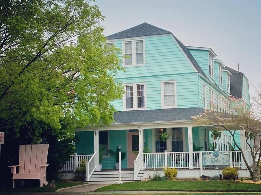 una casa azul con un porche blanco y un banco en Saltwater Inn, en Belmar