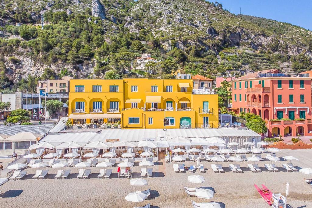 a yellow building with chairs and umbrellas on a beach at Hotel Albatros Varigotti in Varigotti
