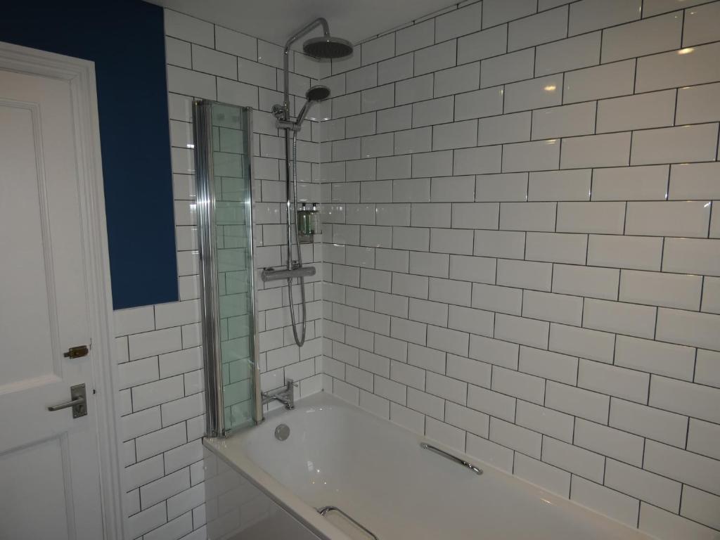 a white tiled bathroom with a tub and a mirror at The Sloop Inn in Kingsbridge