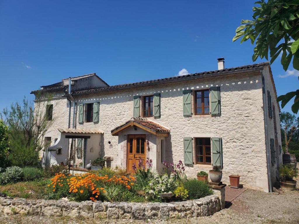 uma casa de pedra branca com janelas verdes e flores em Au Mas de Janita em Cahuzac-sur-Vère