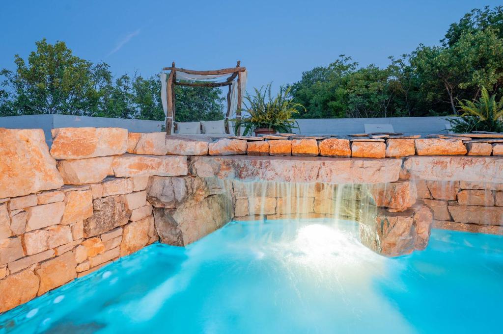 a swimming pool with a stone wall and blue water at Nono Ban Hotel & Villa in Gornji Humac