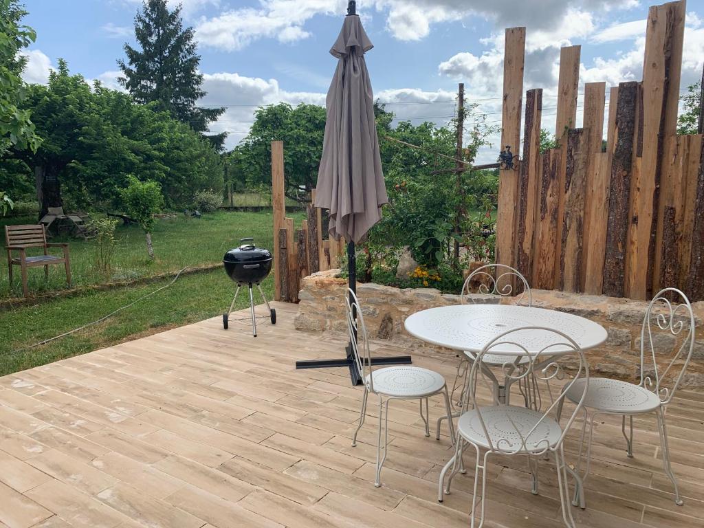 un patio con 2 mesas, una sombrilla y una parrilla en gîte La Longère bleue, en Caylus