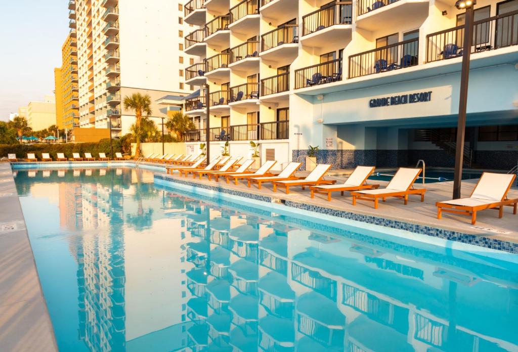 een zwembad met ligstoelen naast een gebouw bij Grande Beach Resort in Myrtle Beach