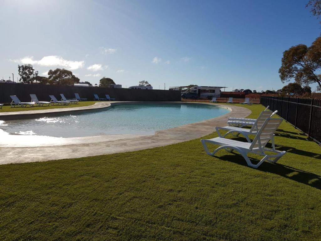 a swimming pool with two white chairs in the grass at BIG4 Stuart Range Outback Resort in Coober Pedy