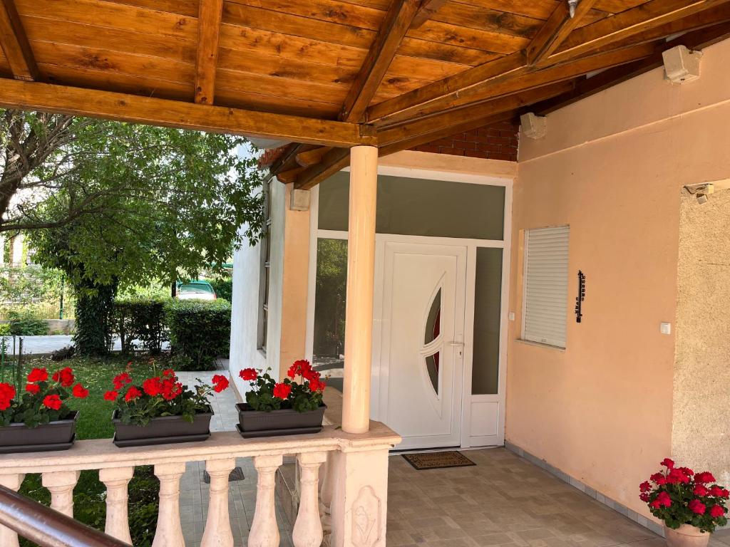 a porch with red flowers and a white door at Apartment Ružica in Sukošan