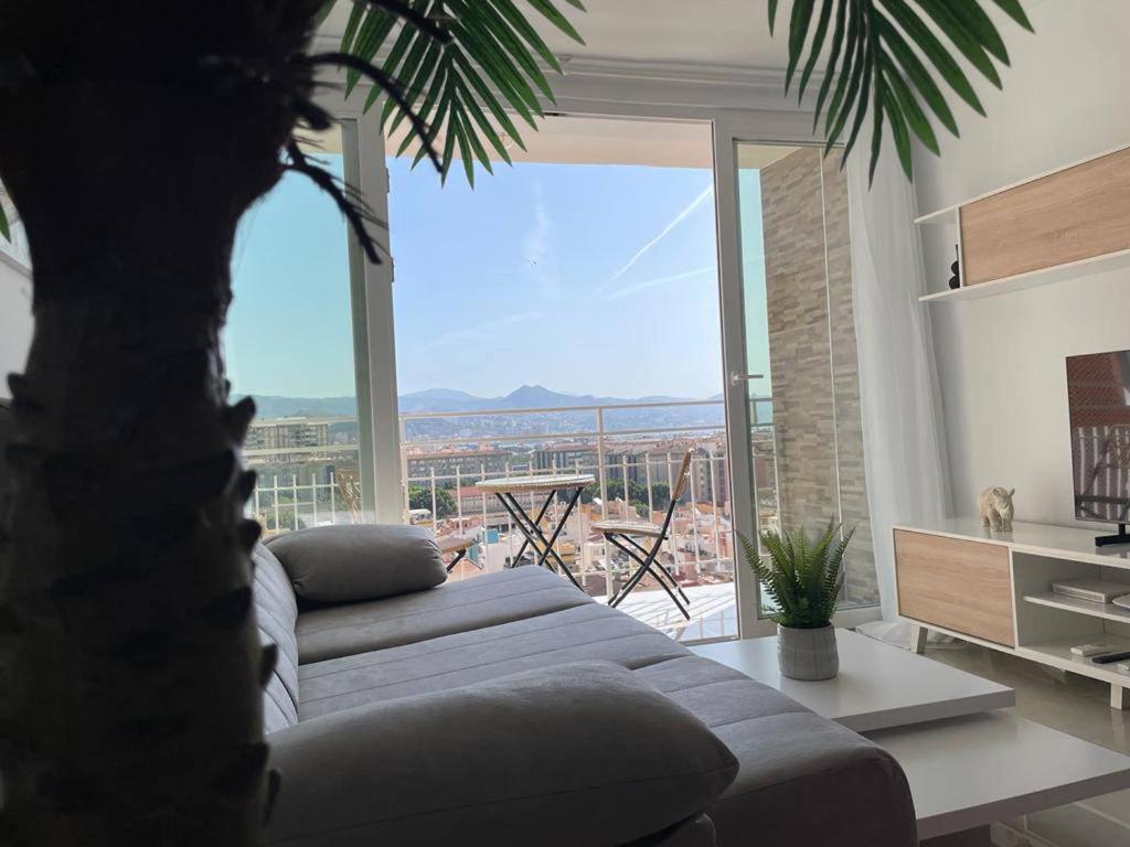 a living room with a couch and a large window at Holidays2Malaga Princesa 3 dormitorios, vistas al mar y montaña, terraza y a 200m a la playa in Málaga