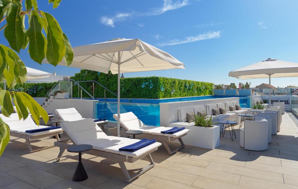 eine Terrasse mit weißen Stühlen, Tischen und einem Sonnenschirm in der Unterkunft H10 Casa de la Plata in Sevilla