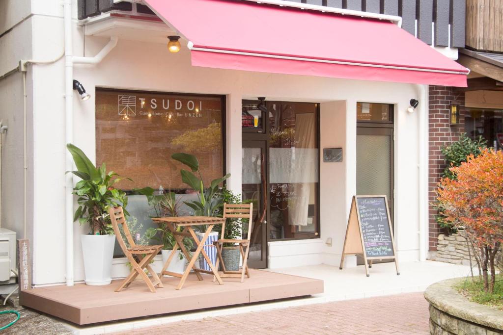 雲仙市にあるTSUDOI guest houseの歩道のピンクの日よけと椅子のあるカフェ