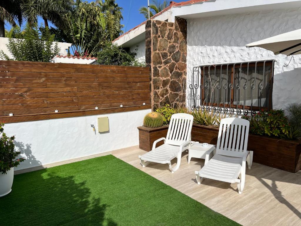 un patio con 2 sillas blancas y un césped verde en Bungalow Yumbo, en Playa del Inglés