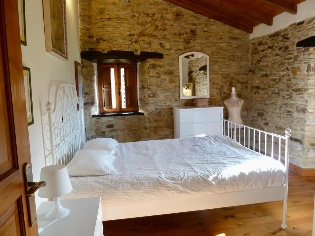 a bedroom with a white bed and a brick wall at Casita feliz entre montañas y cerca del mar in Trabada
