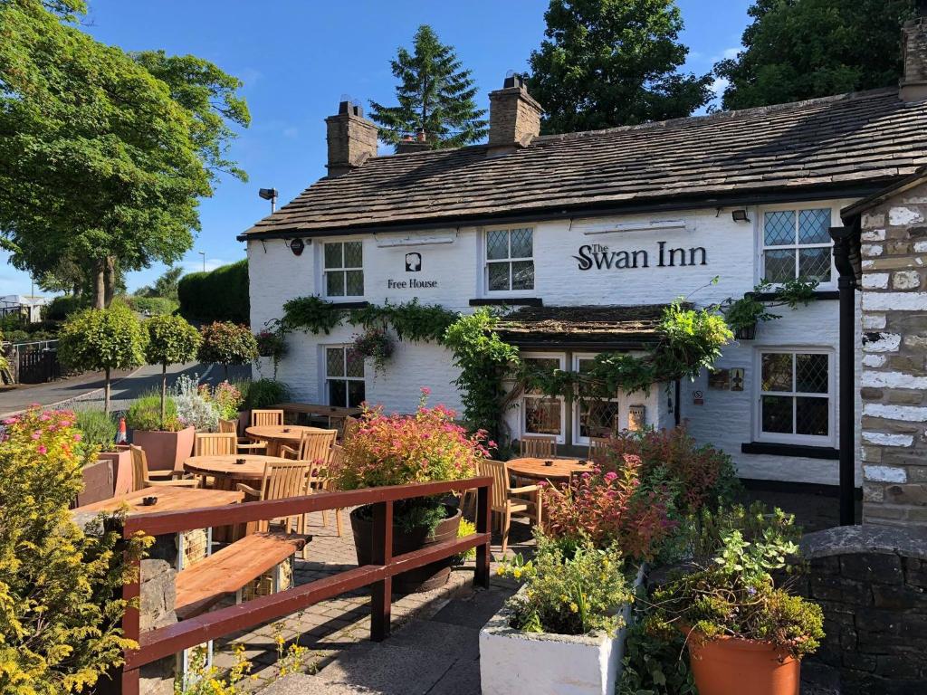 a inn with wooden tables and benches in front of it at The Swan Inn in Highpeak Junction