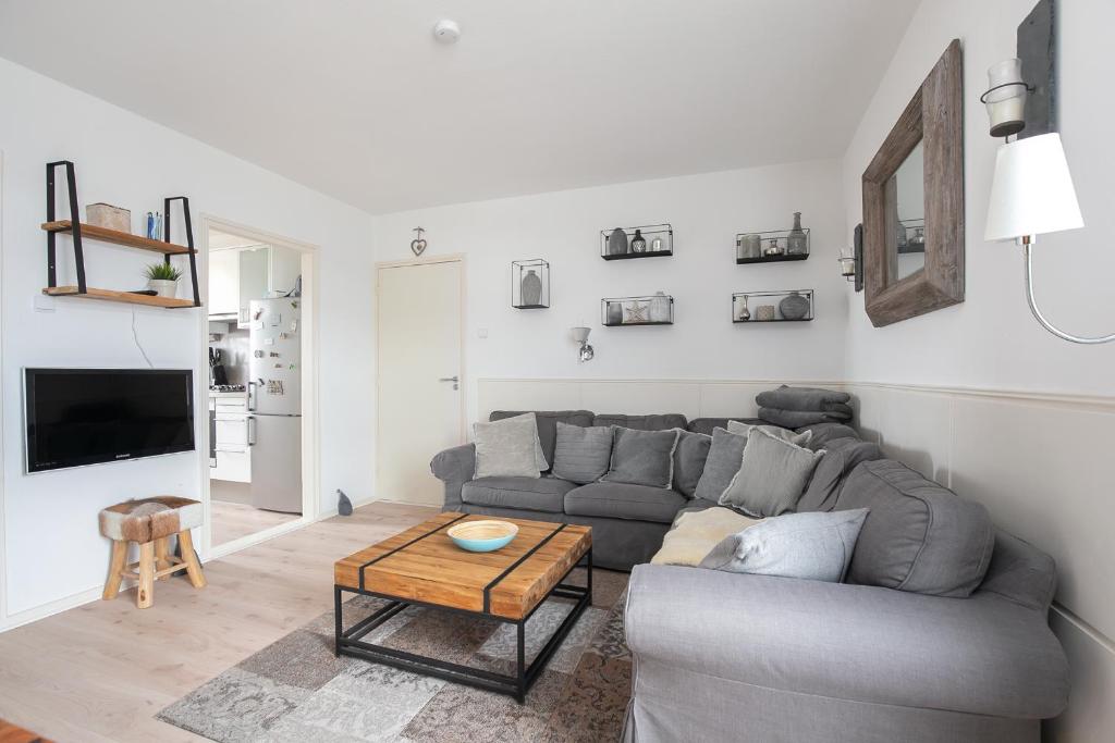 ein Wohnzimmer mit einem grauen Sofa und einem Tisch in der Unterkunft Hello Zeeland - Vakantiehuis Noordstraat 32 in Zoutelande