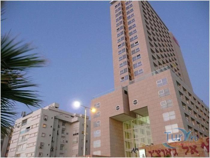 a tall building with a palm tree in front of it at Ezore Yam Apartments - Ben Gurion 99 in Bat Yam