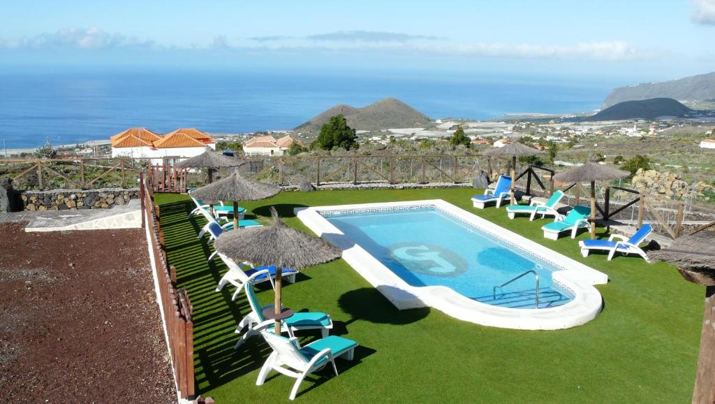 a swimming pool with chairs and umbrellas and the ocean at Apartamentos Fuente La Teja & Spa in Los Llanos de Aridane