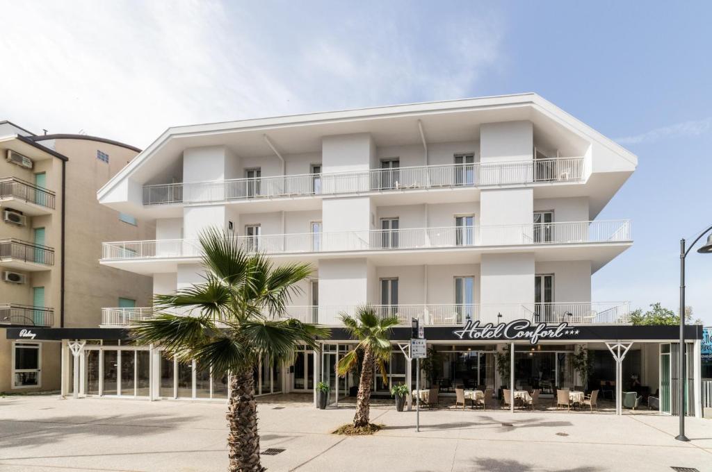 a white building with palm trees in front of it at Hotel Confort in Cattolica