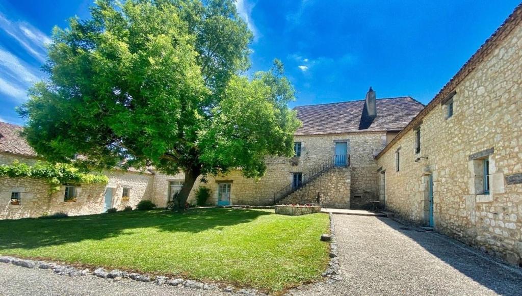 duży kamienny budynek z drzewem na dziedzińcu w obiekcie Chambre d'hôte "la Source" Domaine de Fonpeyroune w mieście Conne-de-Labarde