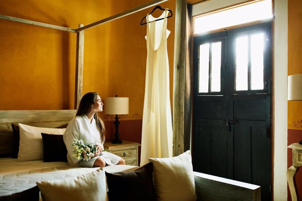 a woman sitting on a bed next to a window at Hotel Hacienda Ticum in Ekmul