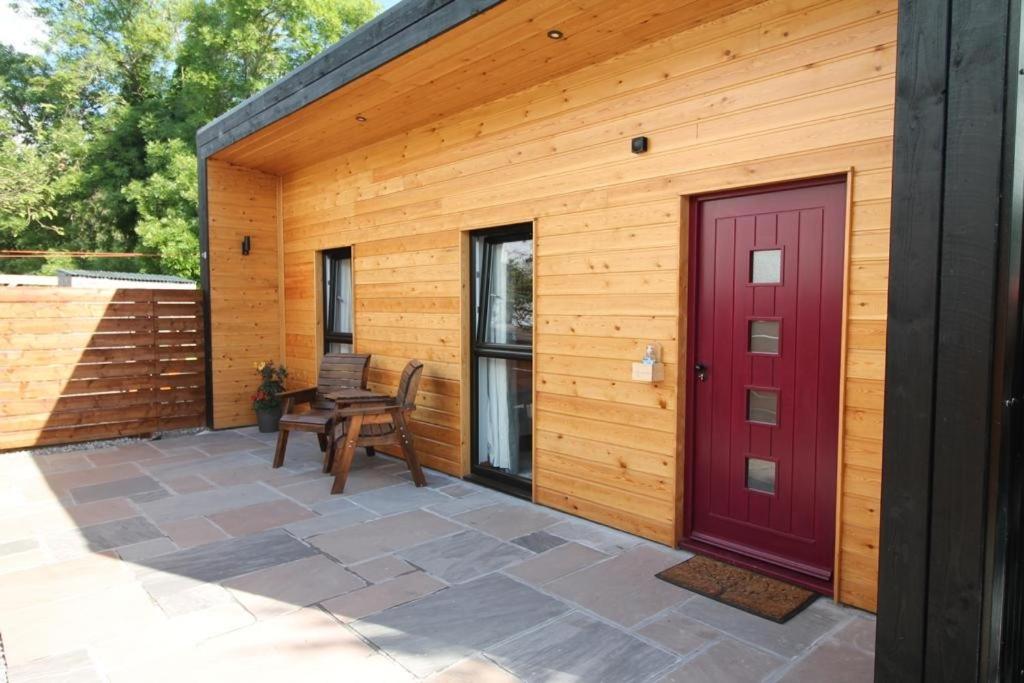 a wooden building with a red door and a bench at The Hide in Ullapool