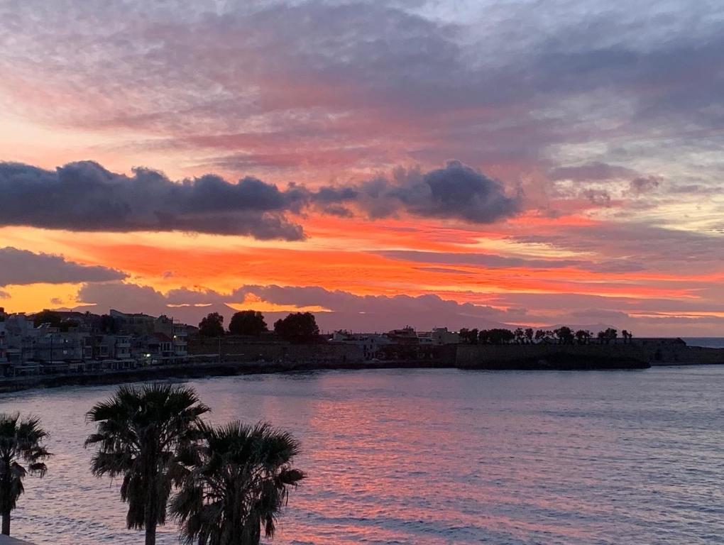 a sunset over a body of water with palm trees at zonapartments A sea view-city center in Chania